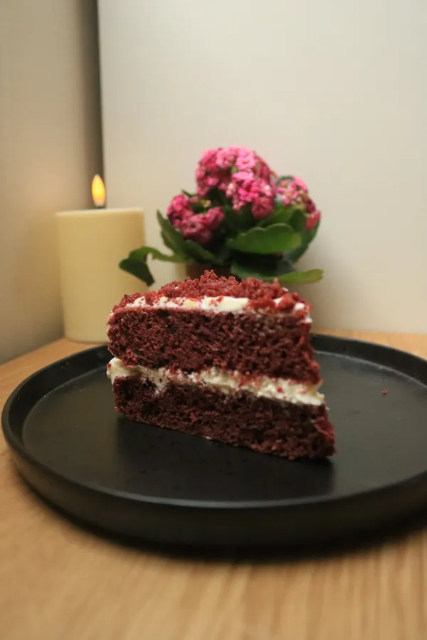 A layered cake slice on a dark plate beside a lit candle and flowers.