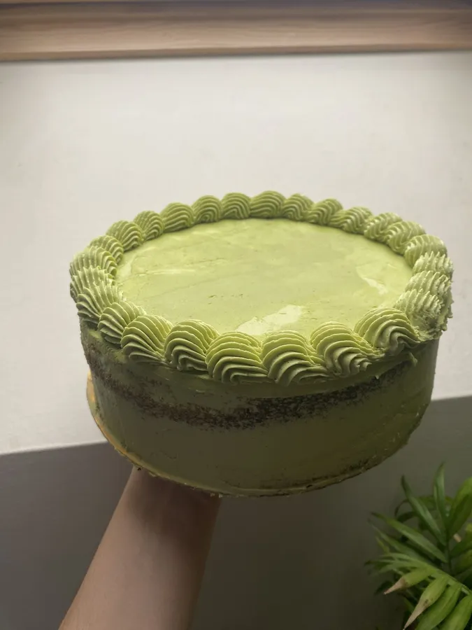 A green-iced layer cake with piped frosting held up to the light.