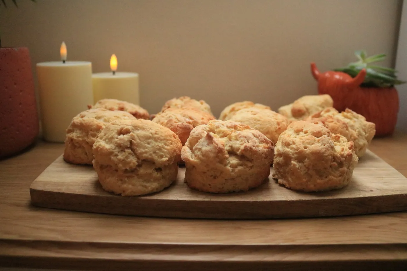 Freshly baked scones arranged on a wooden board between lit candles.