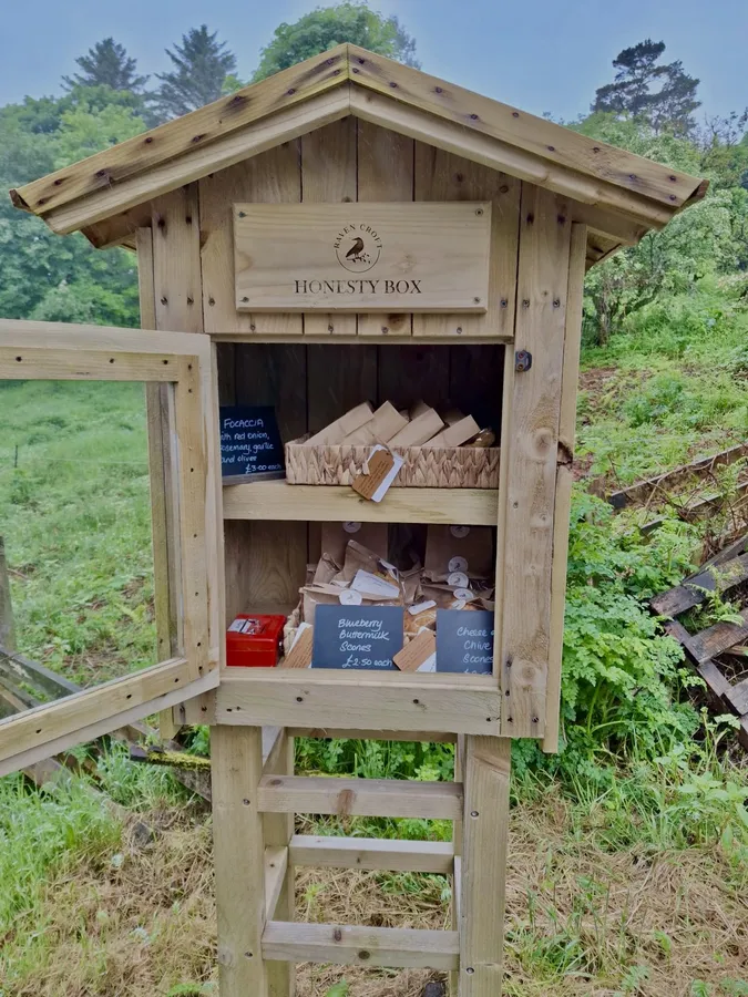 The Raven Croft honesty box: a small wooden hut on ladder-style legs at the roadside, stocked with baked goods.