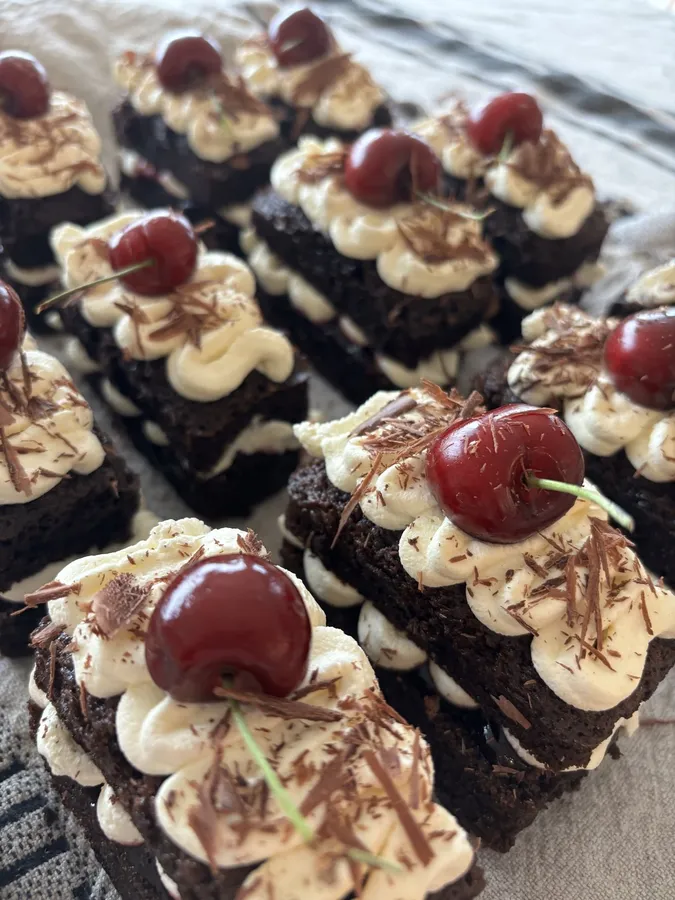 Chocolate cake slices topped with piped cream and whole cherries.