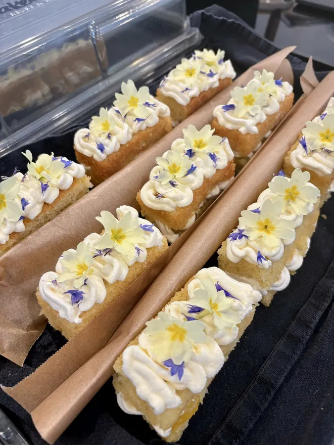 Iced cake slices decorated with piped cream and edible flowers, lined up in a tray.